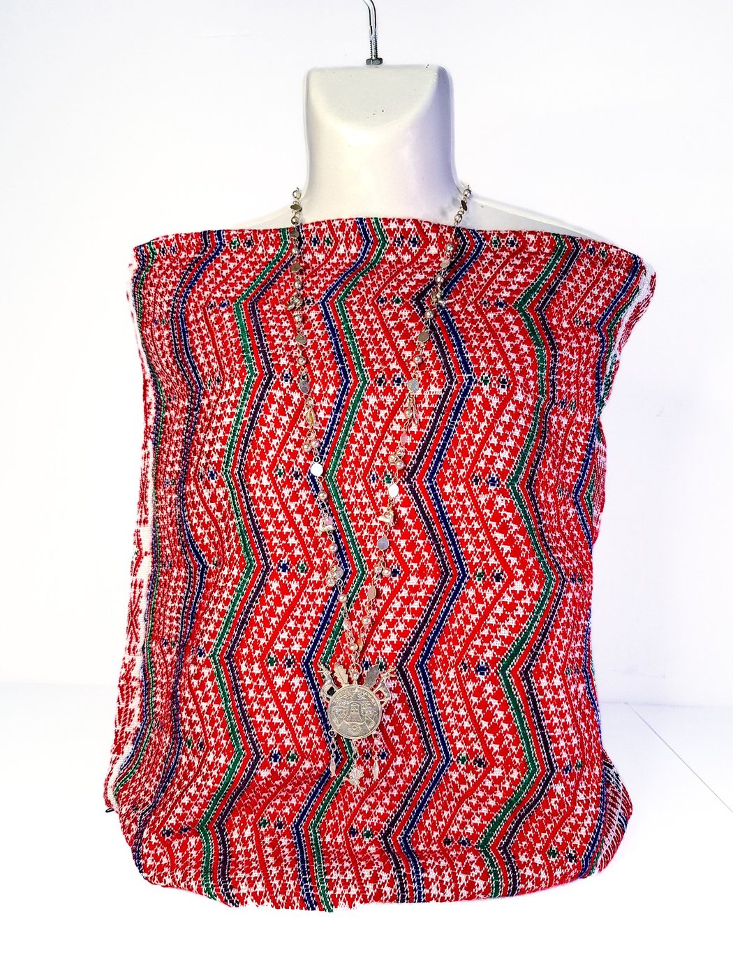 Textil de fondo rojo con motivos en zigzag en azul, verde y negro, colocado sobre un maniquí