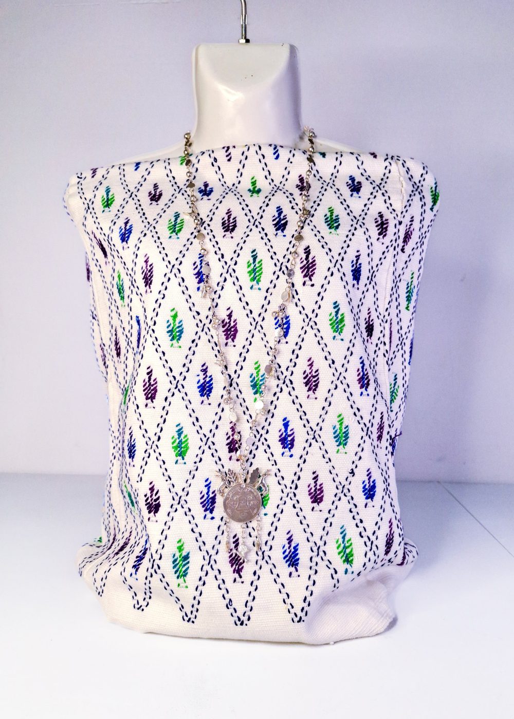Textil blanco con rombos de líneas azul marino y motivos de color colocado sobre un maniquí